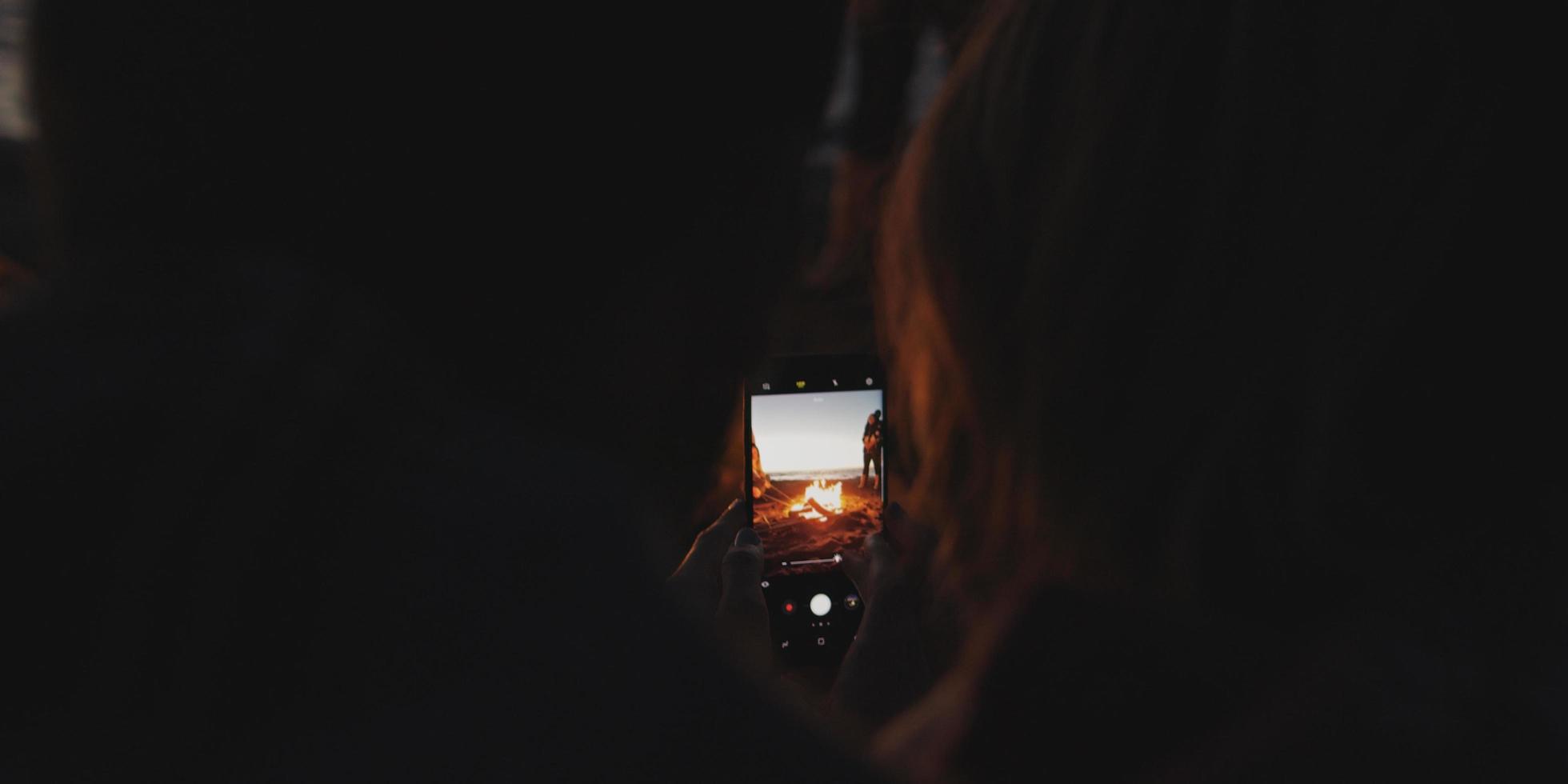 Couple taking photos beside campfire on beach