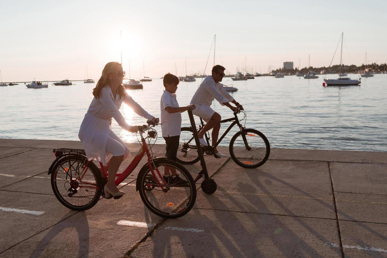 Happy family enjoying a beautiful morning by the sea together, parents riding a bike and their son riding an electric scooter. Selective focus photo