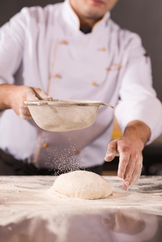 chef rociando harina sobre masa de pizza fresca foto