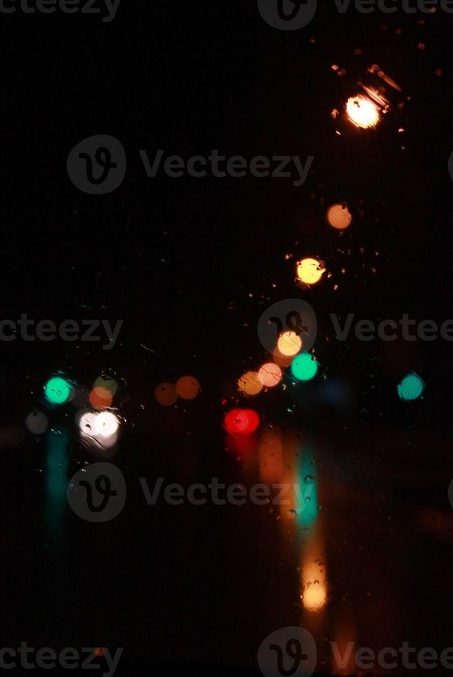 Car traffic lights bokeh through rainy window glass on black background. Defocused city night colorful round lights. photo