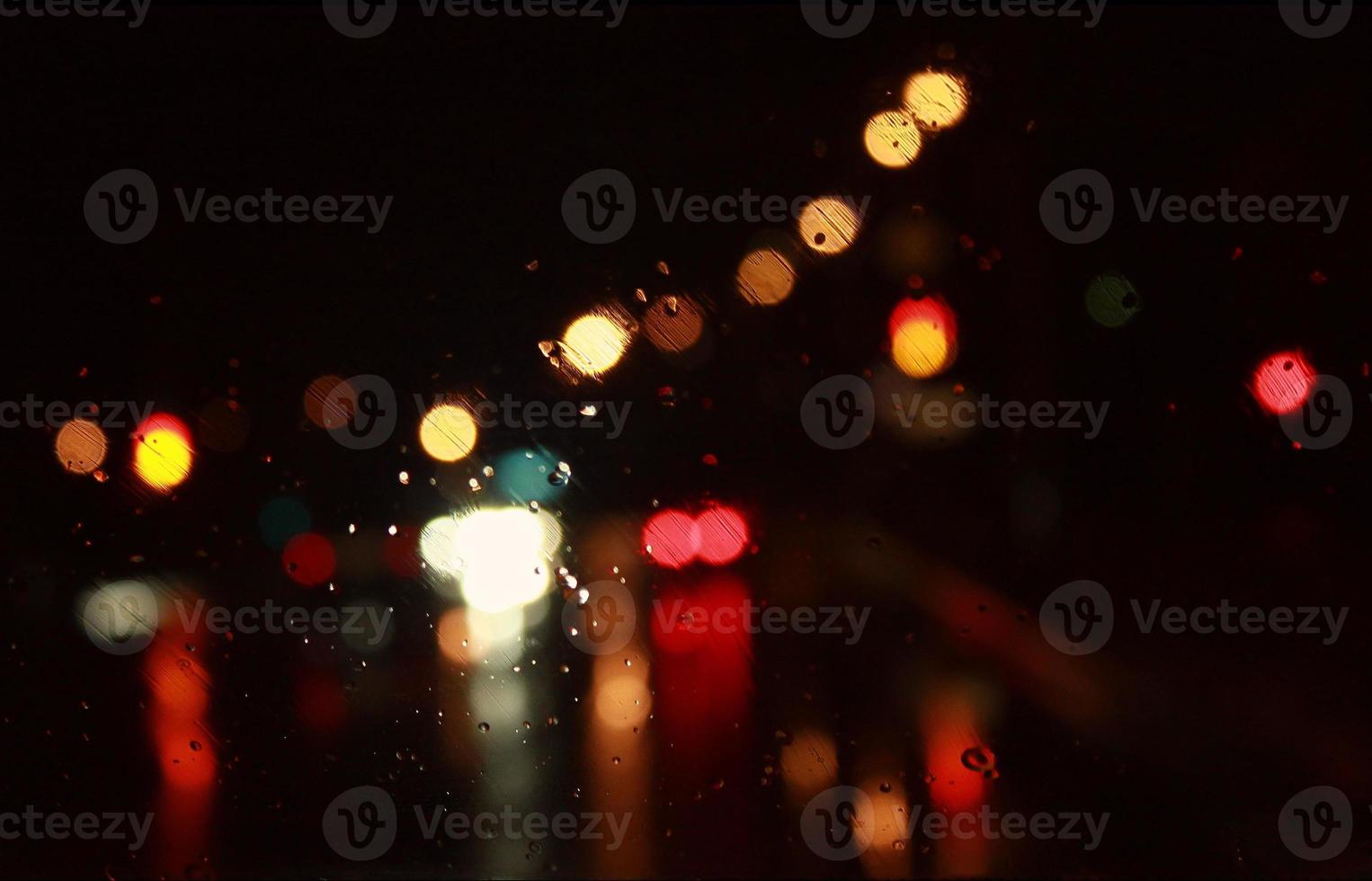 Car traffic lights bokeh through rainy window glass on black background. Defocused city night colorful round lights. photo