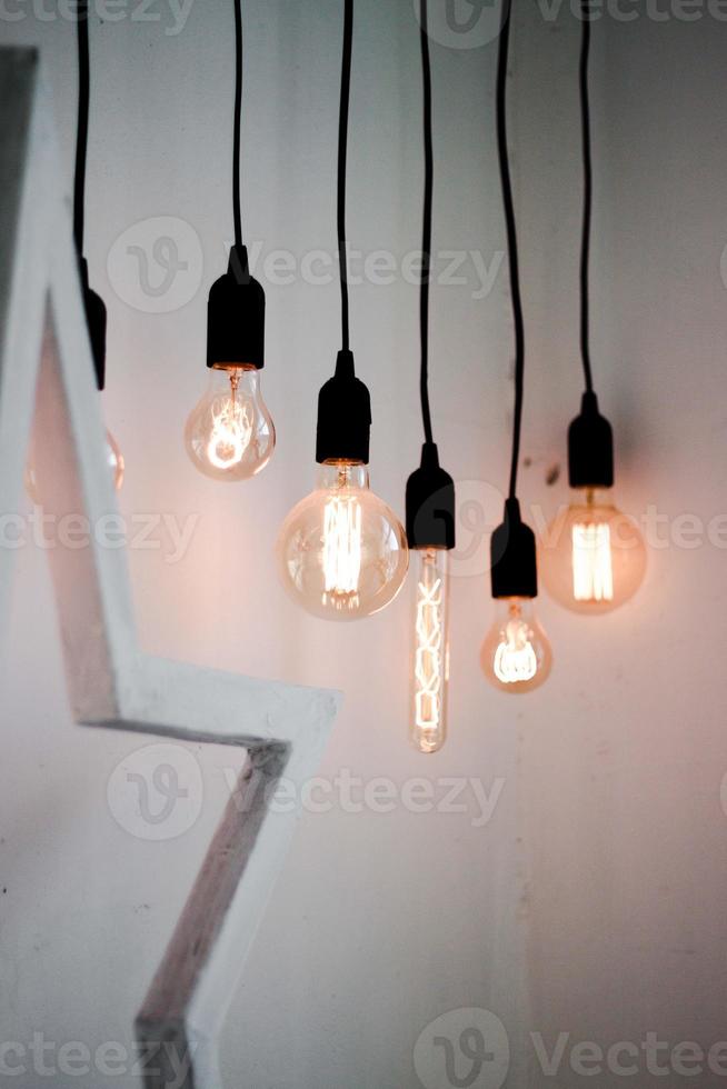 Hanging edison light bulbs on black strings on white wall background photo