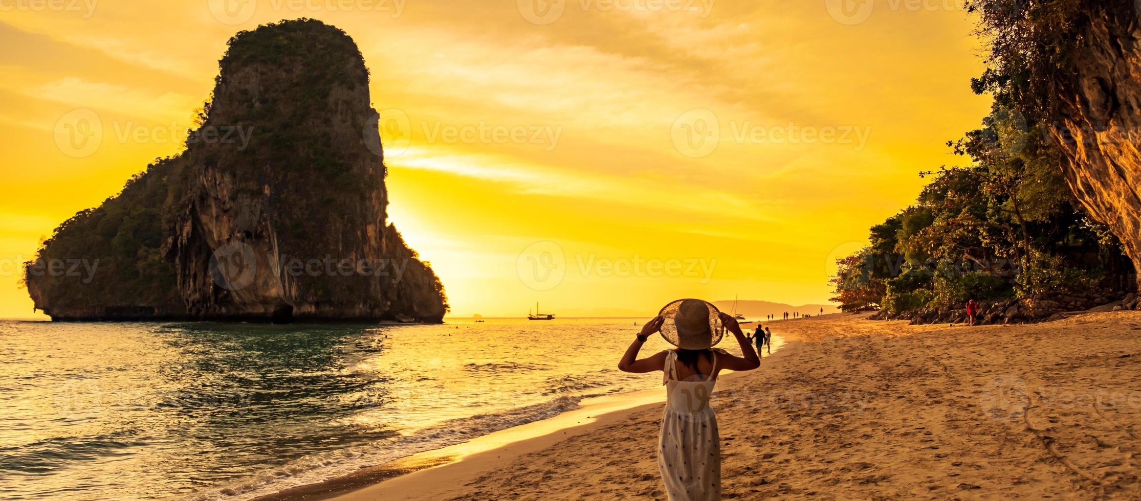 mujer turista con vestido blanco y sombrero caminando en la playa de la cueva de phra nang al atardecer, railay, krabi, tailandia. concepto de vacaciones, viajes, verano, pasión por los viajes y vacaciones foto