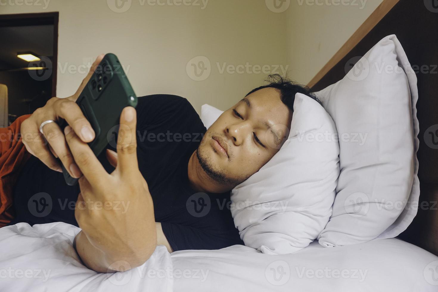 Tired young man checking on his phone while lying in bed photo