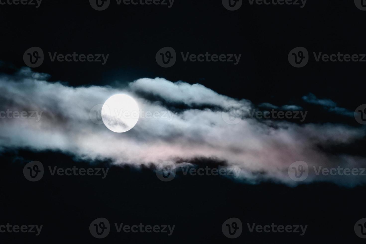 Full moon in the night sky hidden behind clouds tinted with sunset light photo