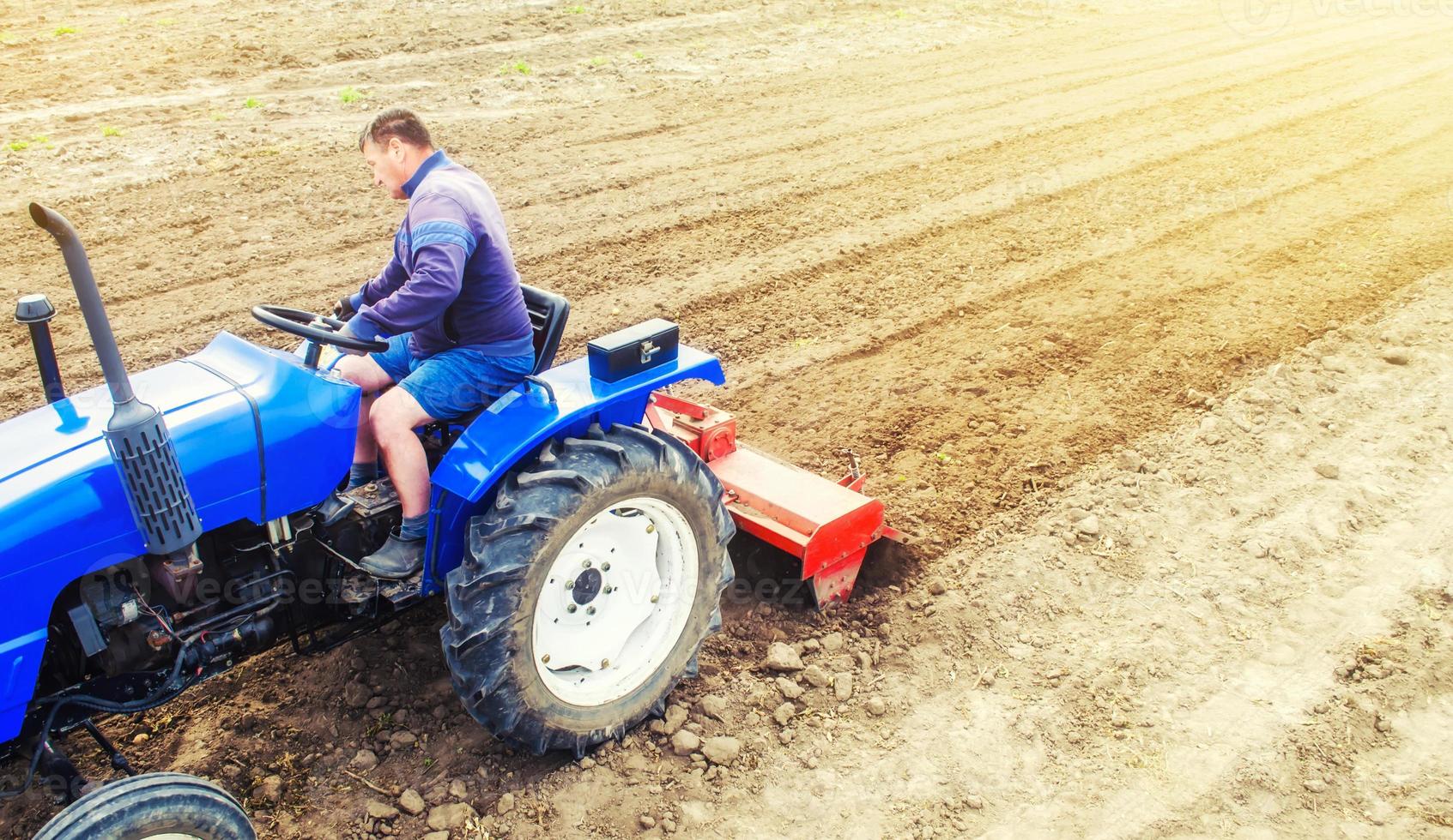 A farmer on a tractor cultivates a farm field. Field land preparation for new crop planting. Grinding and loosening soil, removing plants and roots from past harvest. Cultivation equipment. photo