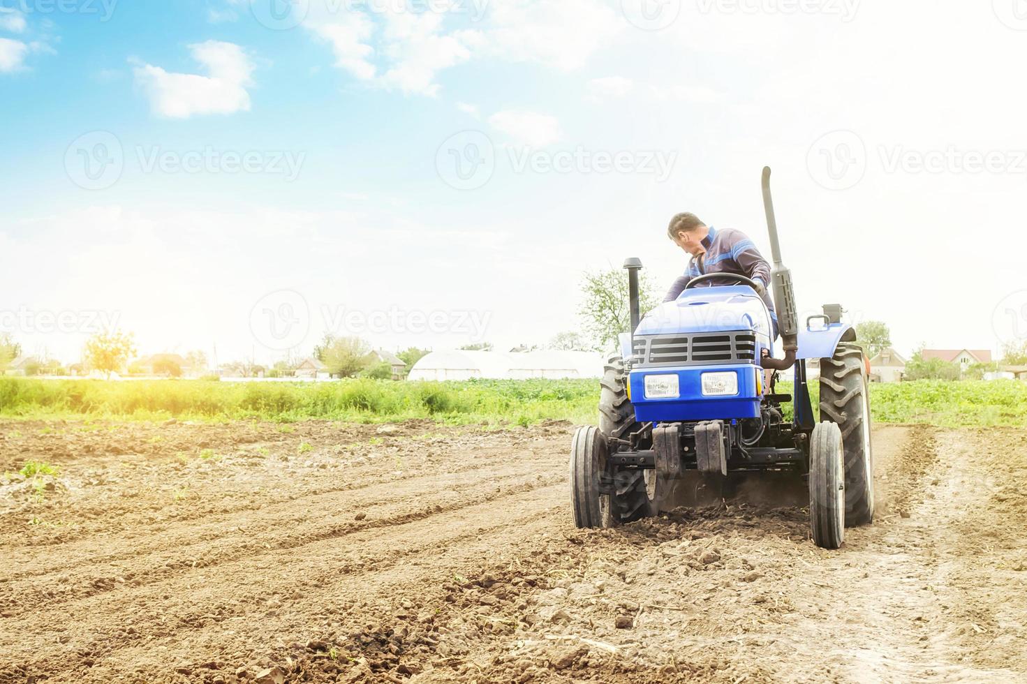 Farmer on a tractor with milling machine loosens, grinds and mixes soil. Loosening surface, cultivating the land for further planting. Farming and agriculture. Use of agricultural machinery on a farm. photo