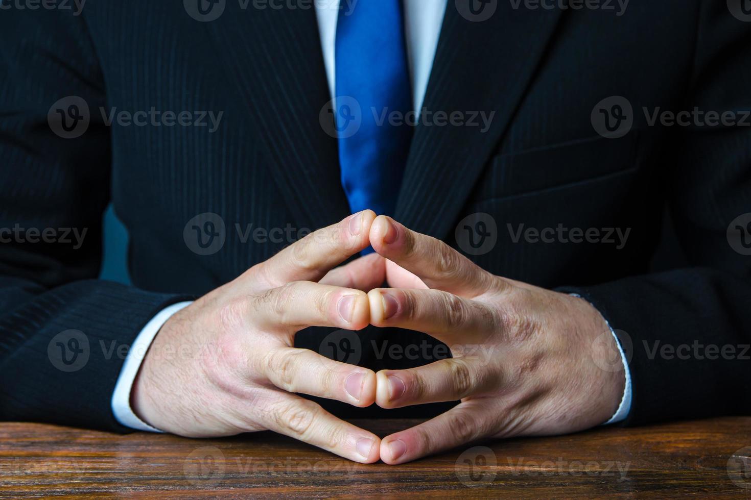 A man sits with his hands in lock. Gesture of strength consolidation and deliberation. Peace of mind and cold calculation. Conflict resolution, search for a compromise. Finding consensus. In thought photo