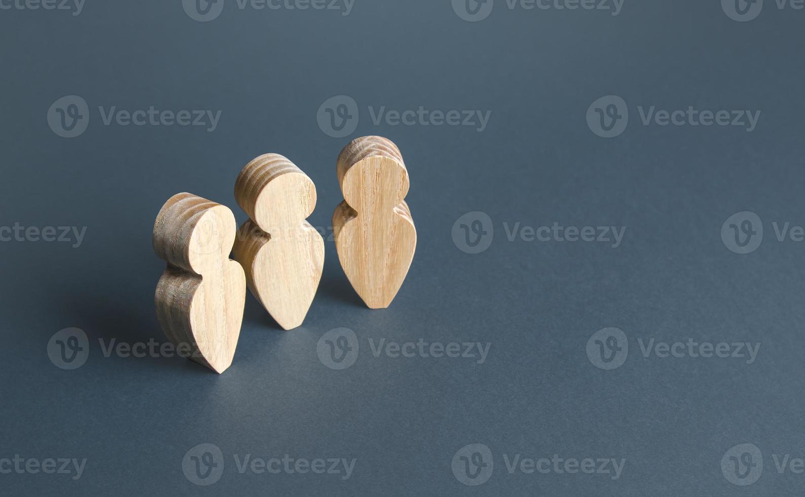 Three wooden human figurines on a gray background. Communication and discussion. Social Meeting. Assistance, cooperation and collaboration. photo