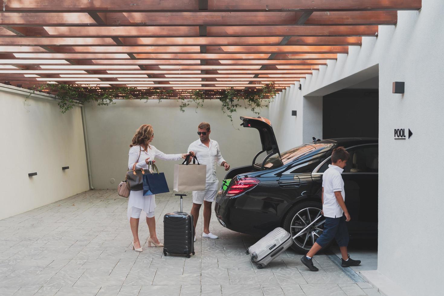 A photo of a modern family carrying suitcases from a garage to their luxury seaside home during a vacation. Vacation concept. Selective focus