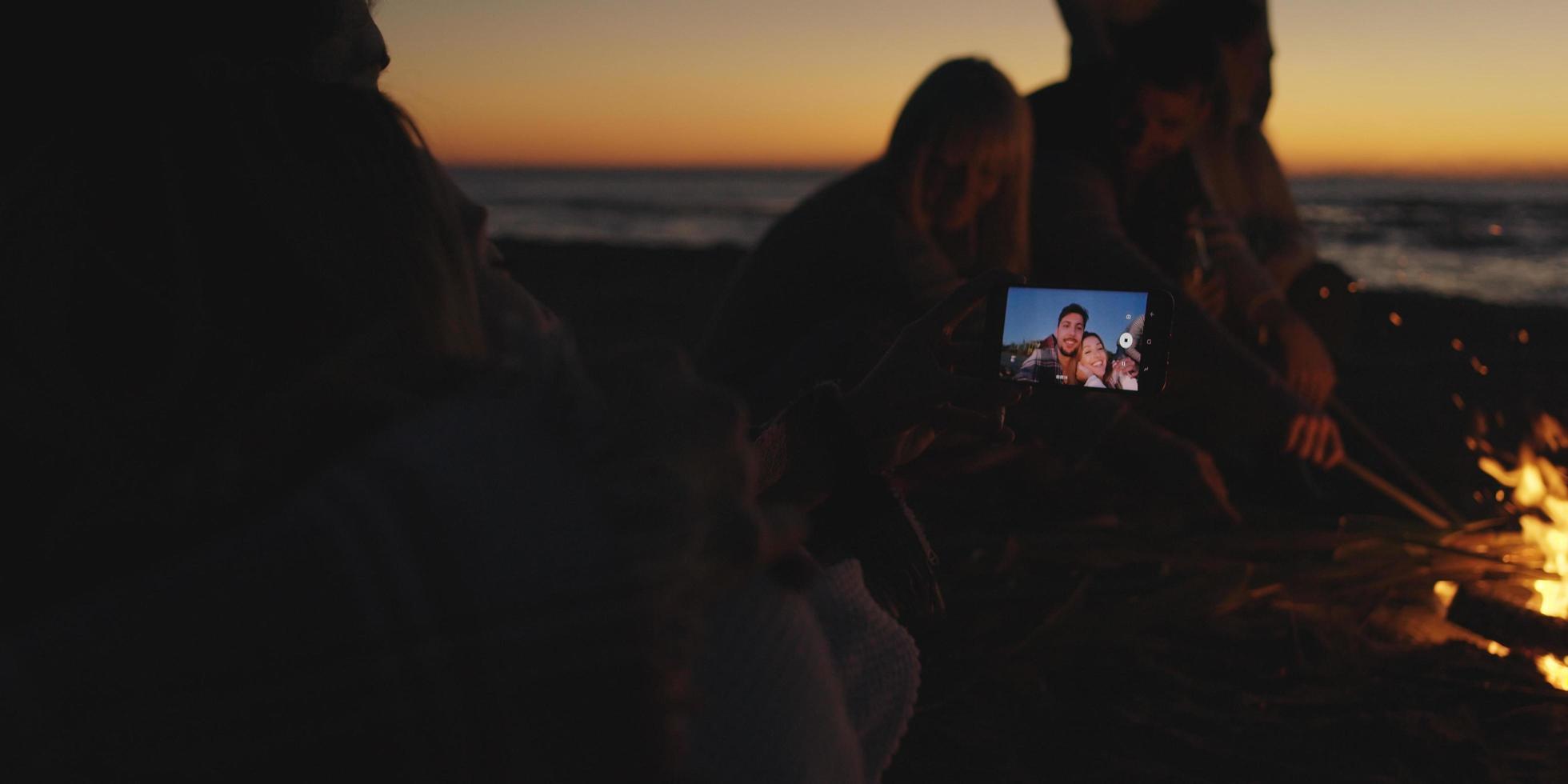 Couple taking photos beside campfire on beach