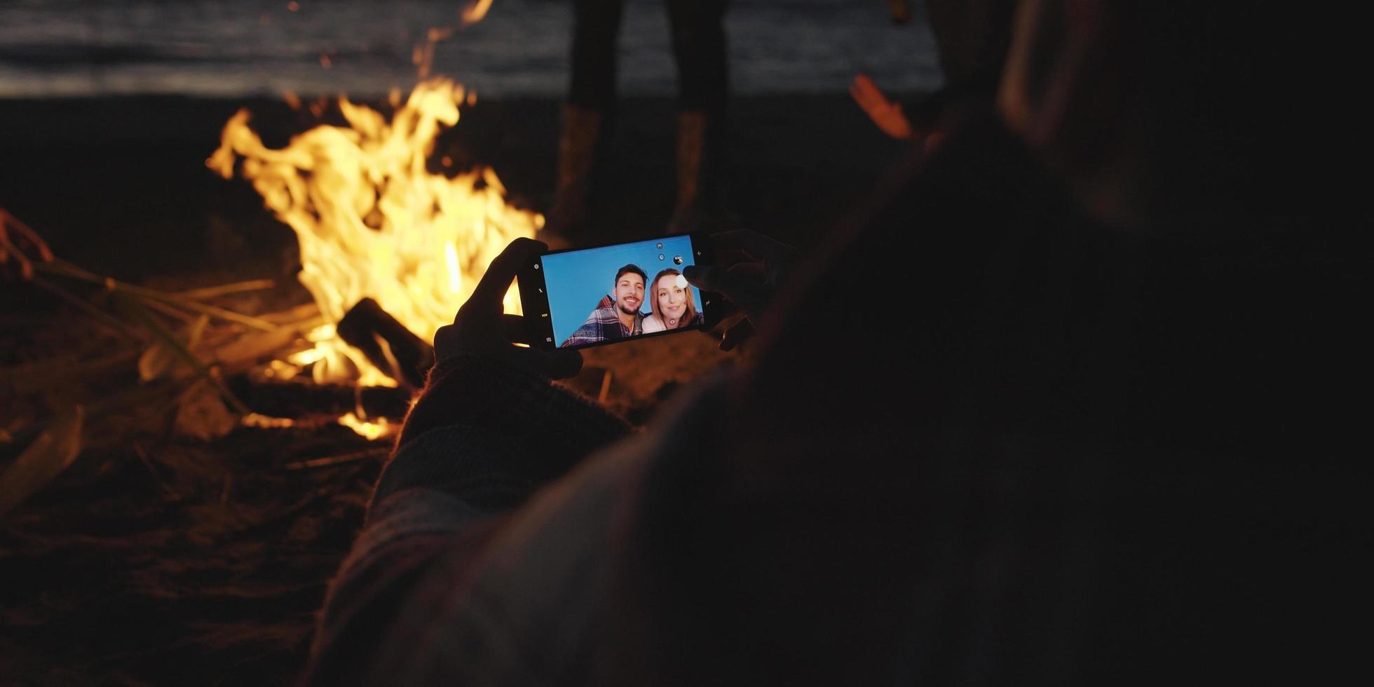 Couple taking photos beside campfire on beach