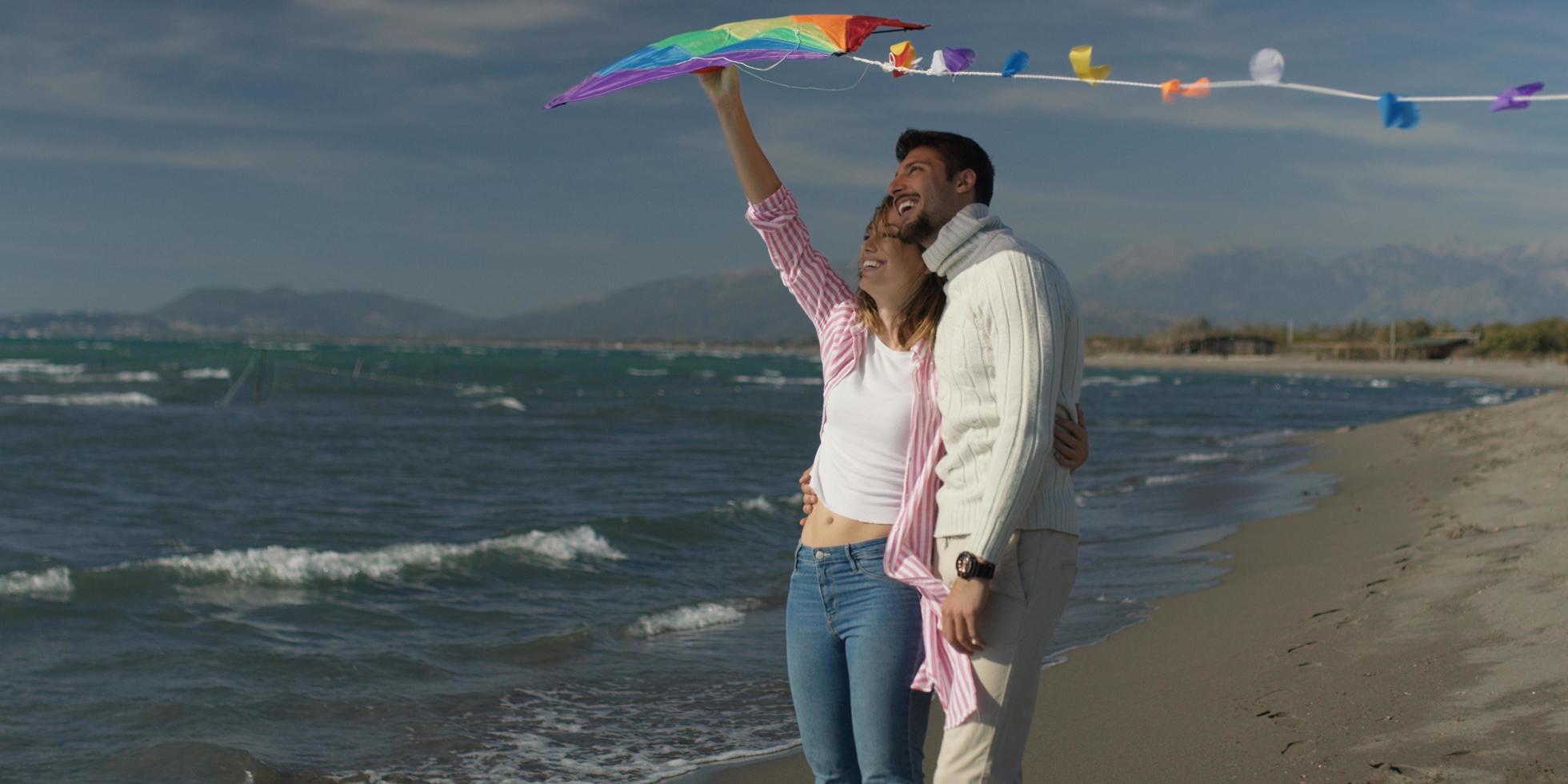 pareja feliz divirtiéndose con cometa en la playa foto