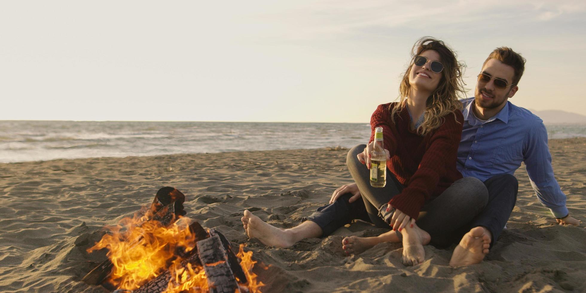 Loving Young Couple Sitting On The Beach beside Campfire drinking beer photo