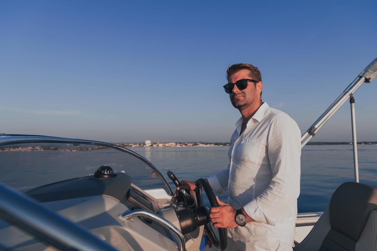 A determined senior businessman in casual clothes and sunglasses enjoys his vacation driving a luxury boat at sunset. Selective focus photo