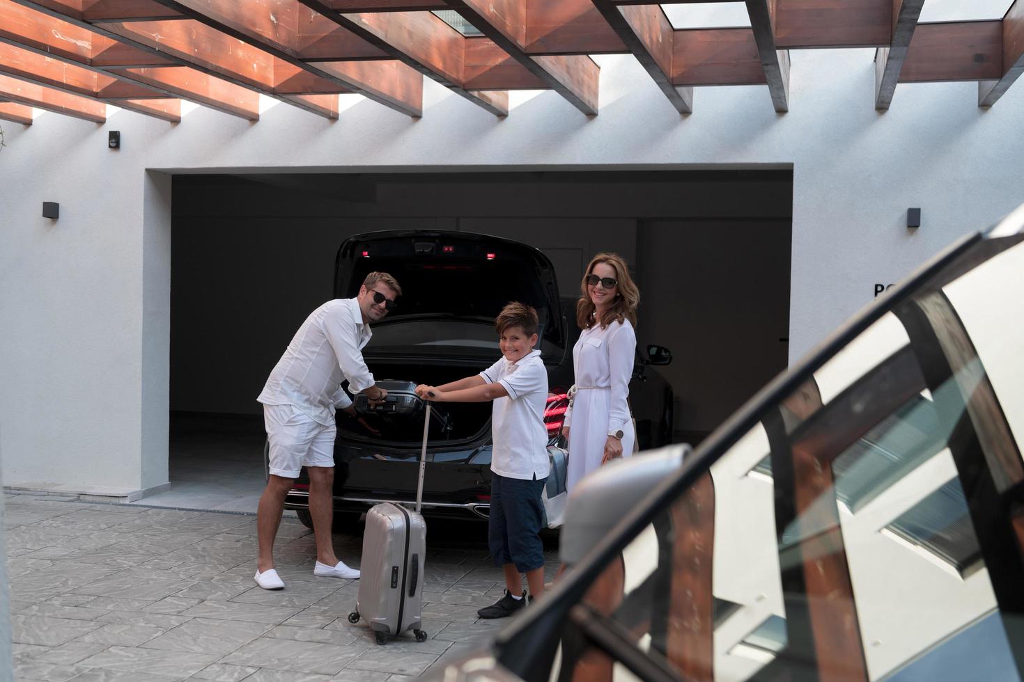 A photo of a modern family carrying suitcases from a garage to their luxury seaside home during a vacation. Vacation concept. Selective focus