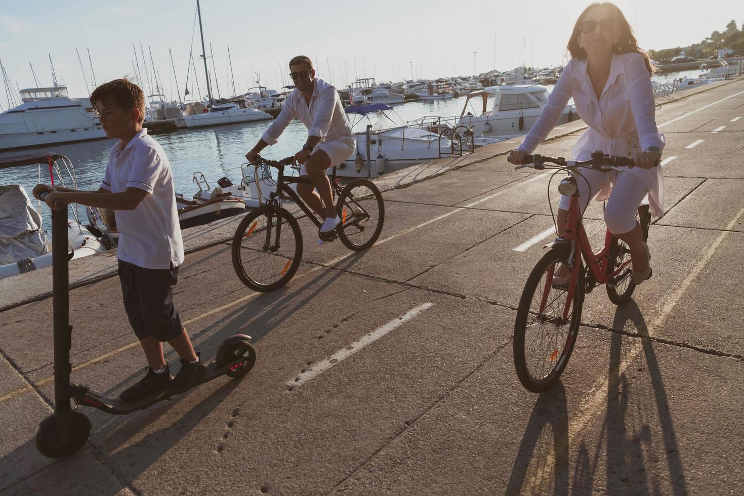 familia feliz disfrutando juntos de una hermosa mañana junto al mar, padres montando en bicicleta y su hijo montando una scooter eléctrica. enfoque selectivo foto