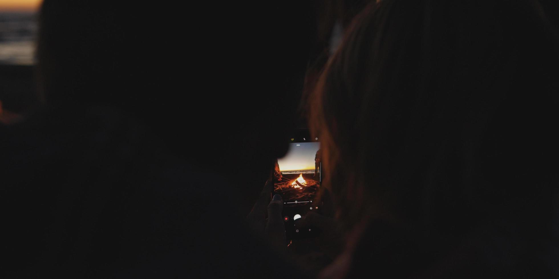 Couple taking photos beside campfire on beach