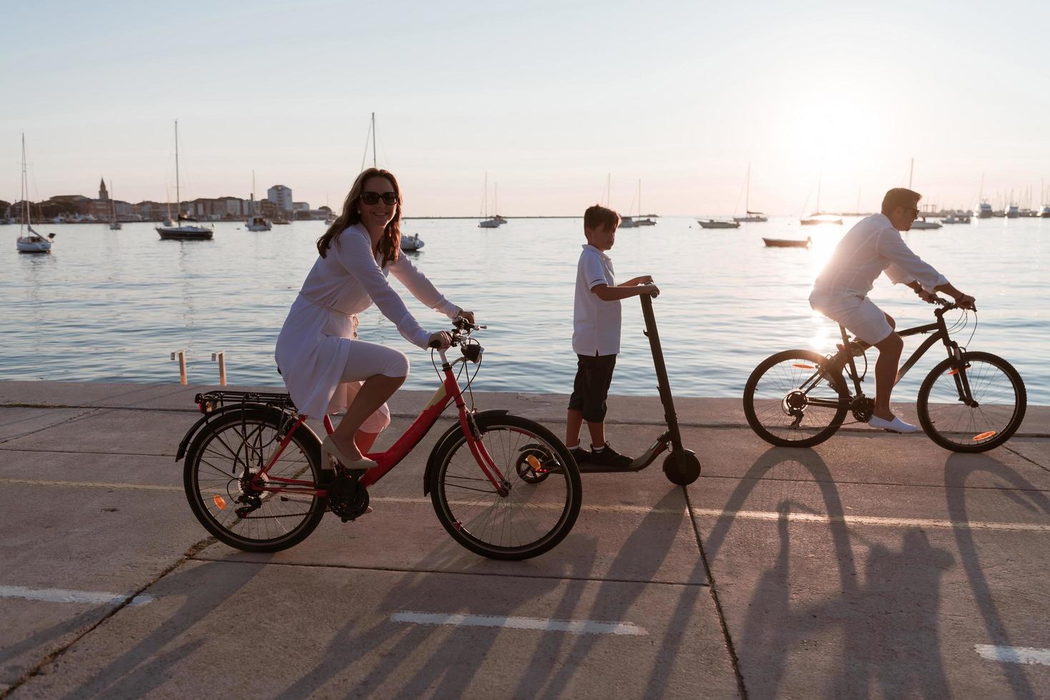 Happy family enjoying a beautiful morning by the sea together, parents riding a bike and their son riding an electric scooter. Selective focus photo