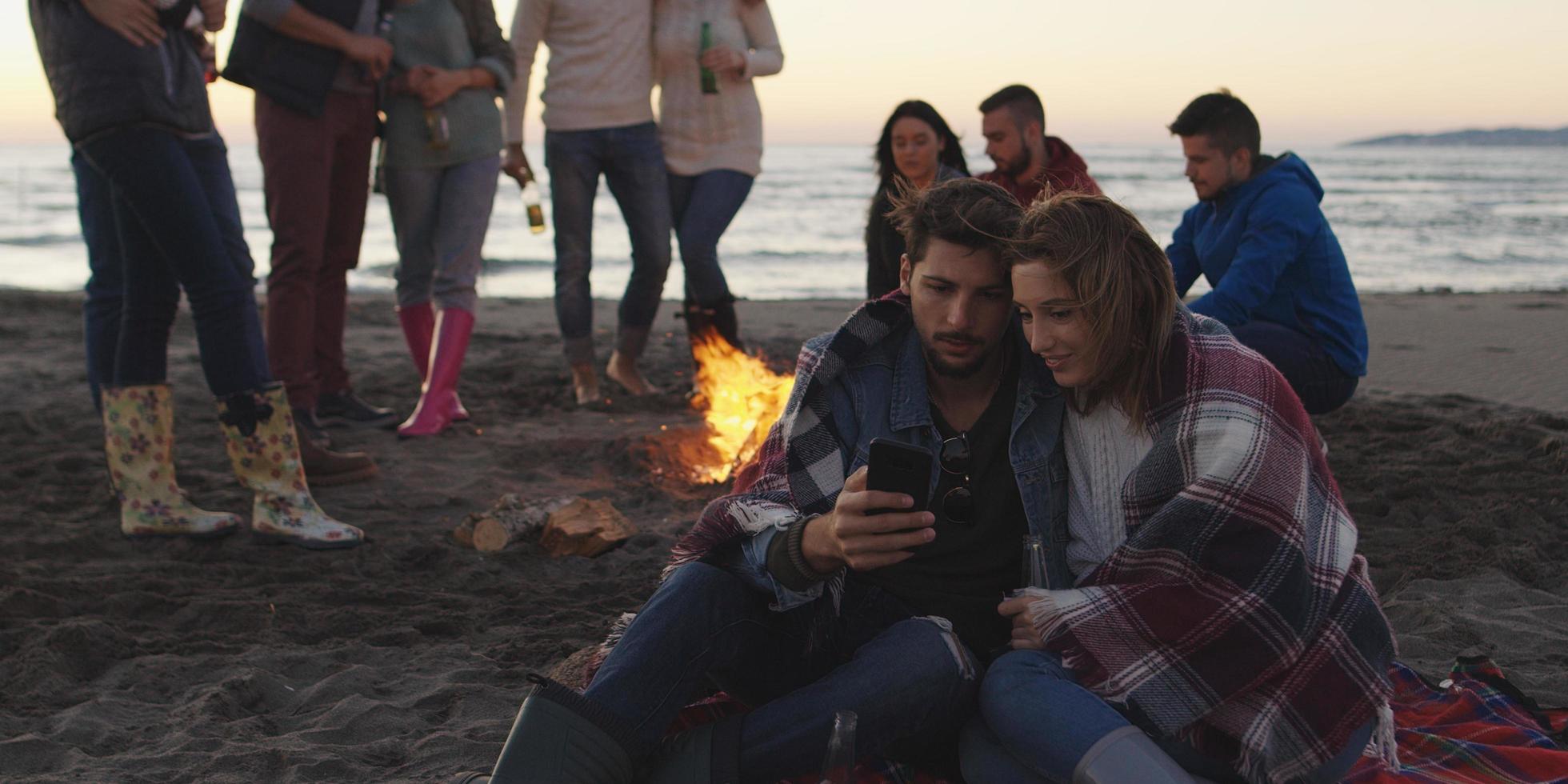Couple enjoying bonfire with friends on beach photo