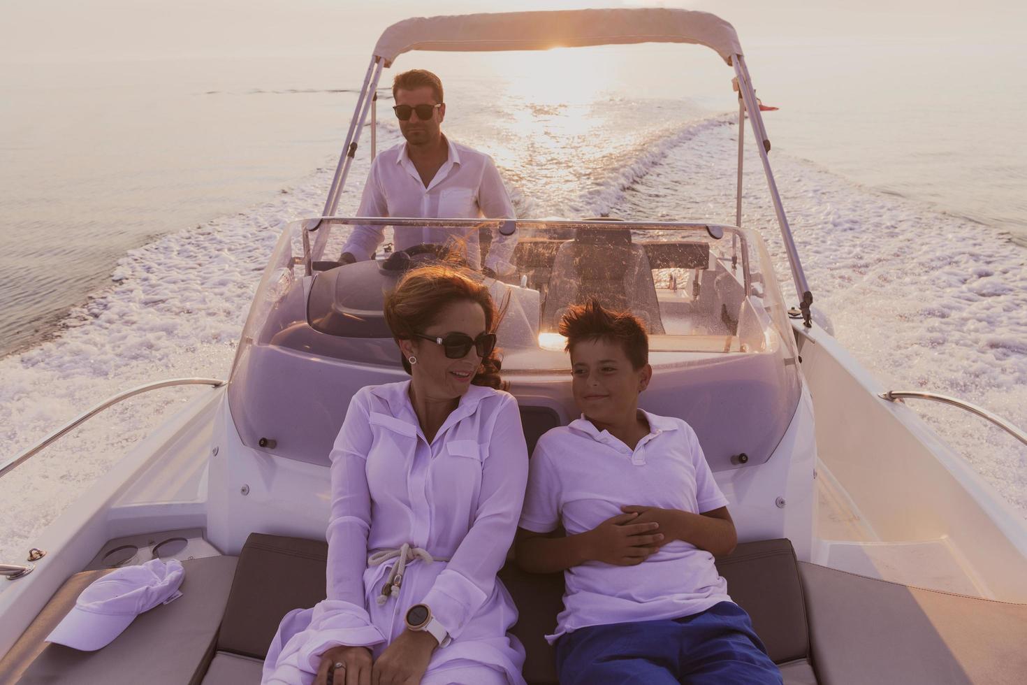 una pareja mayor con ropa informal con su hijo disfruta mientras viaja en un bote en el mar al atardecer. el concepto de una familia feliz. enfoque selectivo foto