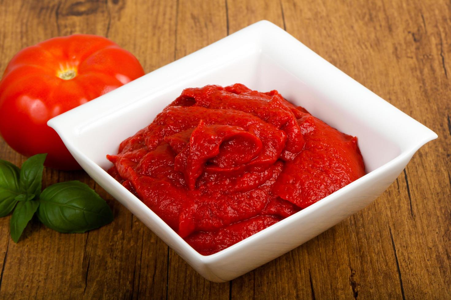 Tomato paste in a bowl on wooden background photo