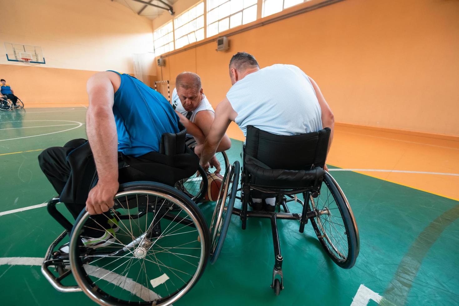 Disabled War veterans mixed race and age basketball teams in wheelchairs playing a training match in a sports gym hall. Handicapped people rehabilitation and inclusion concept photo