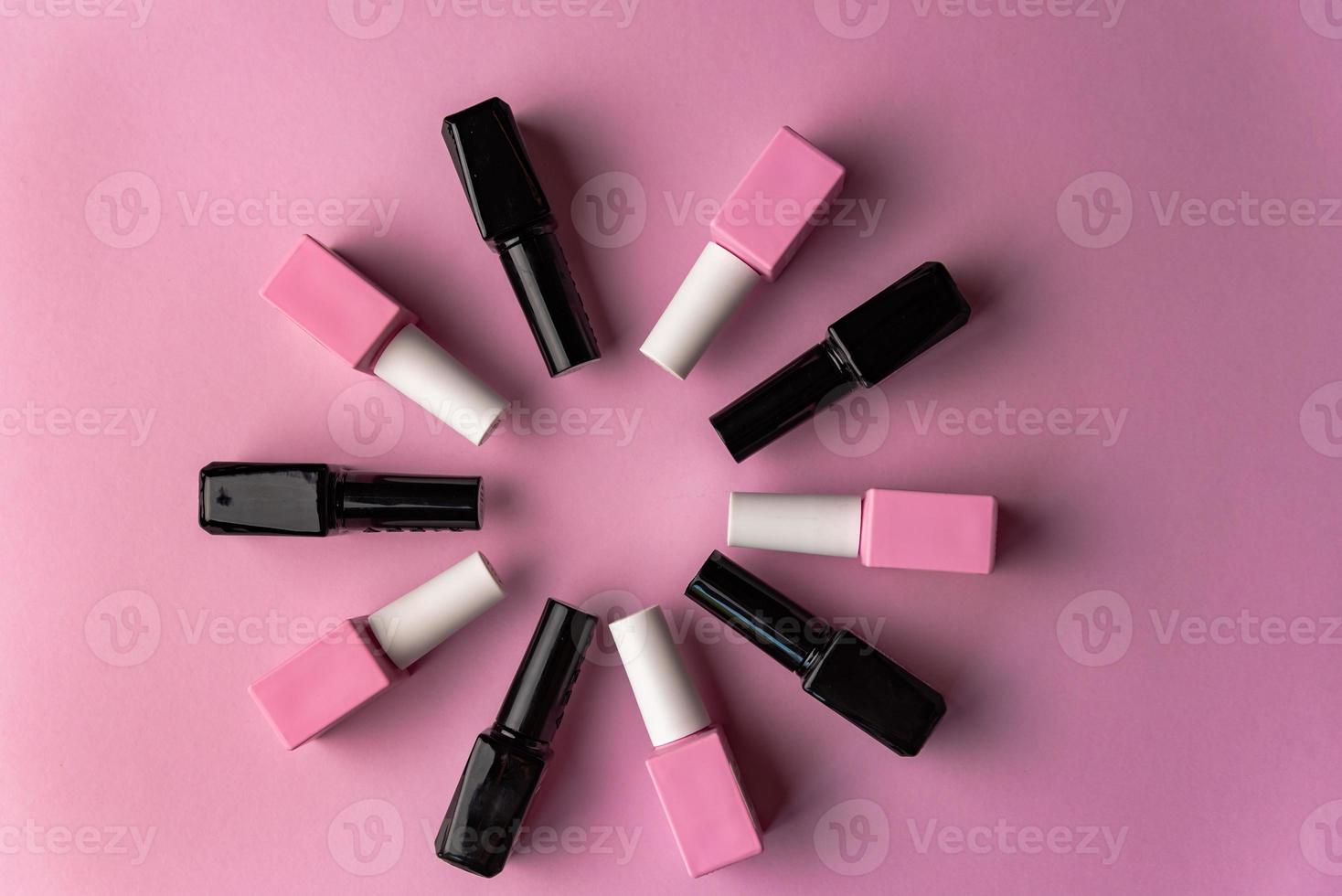 Set of vials with colorful nail lacquer placed in circle on pink background photo