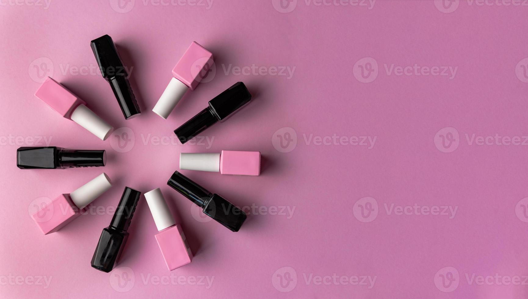 Set of vials with colorful nail lacquer placed in circle on pink background photo