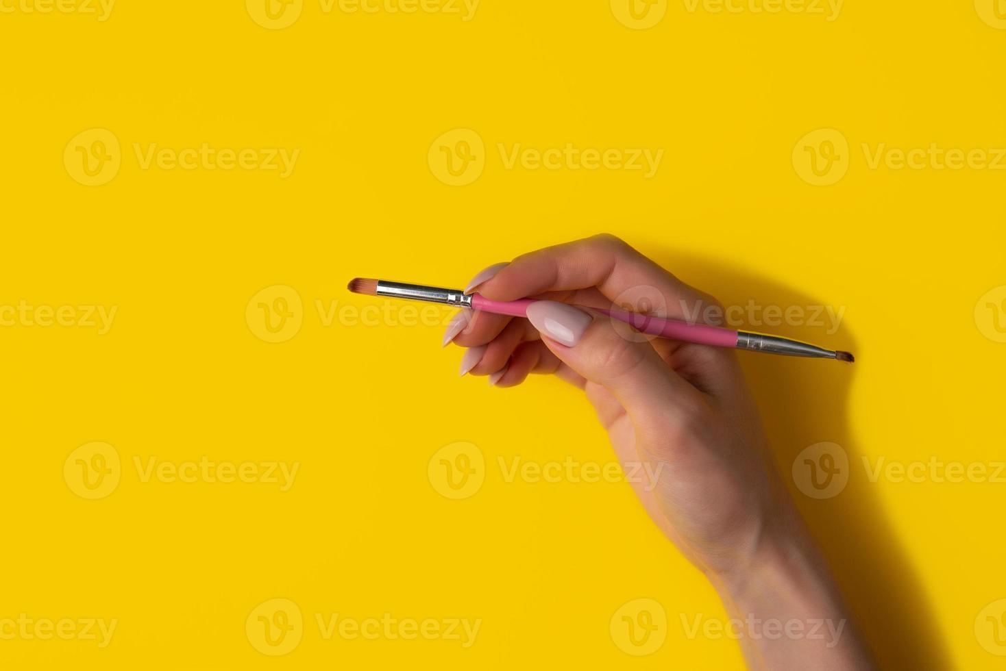 Female hand with a brush on a yellow background, top view photo