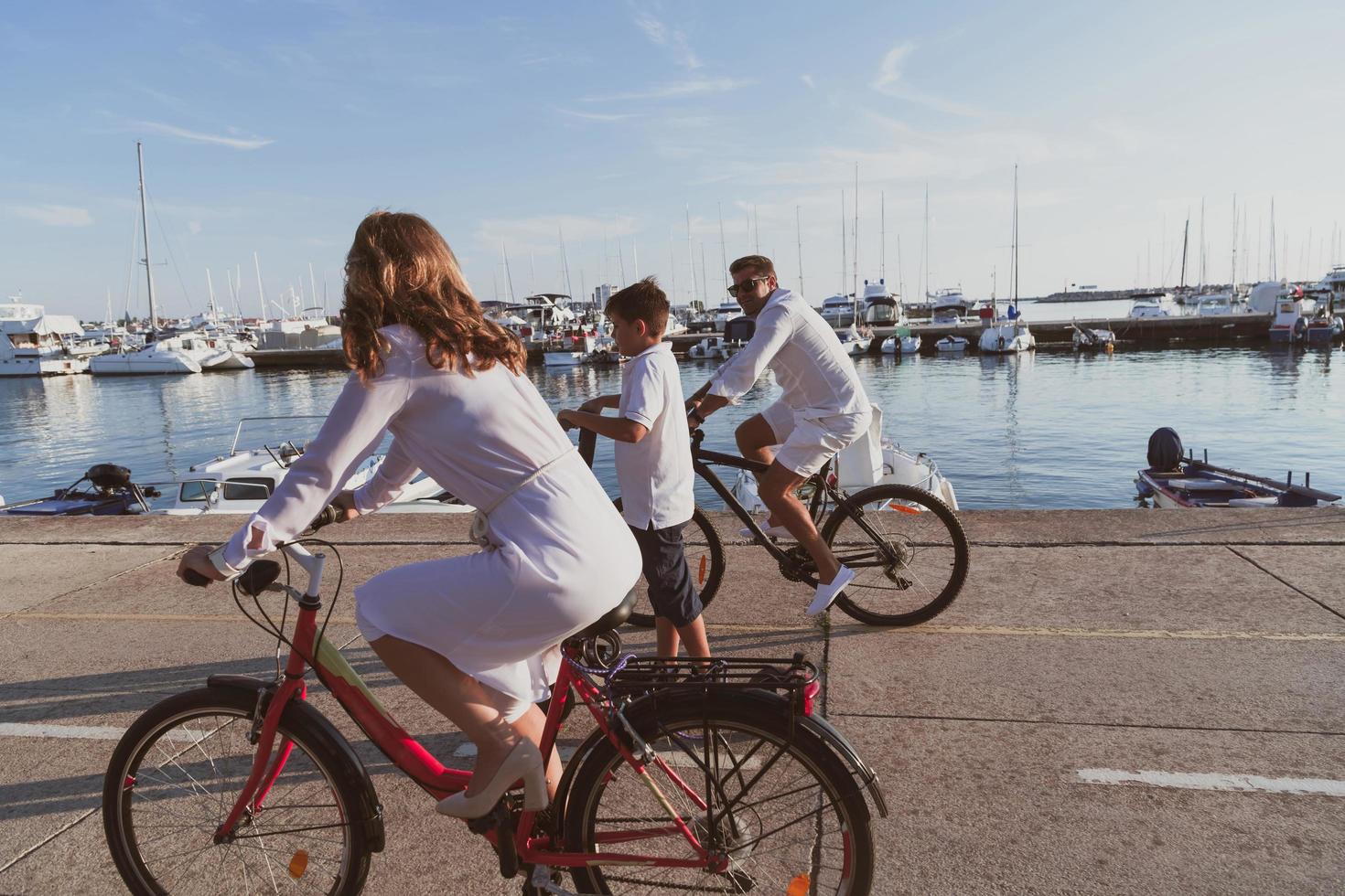 Happy family enjoying a beautiful morning by the sea together, parents riding a bike and their son riding an electric scooter. Selective focus photo
