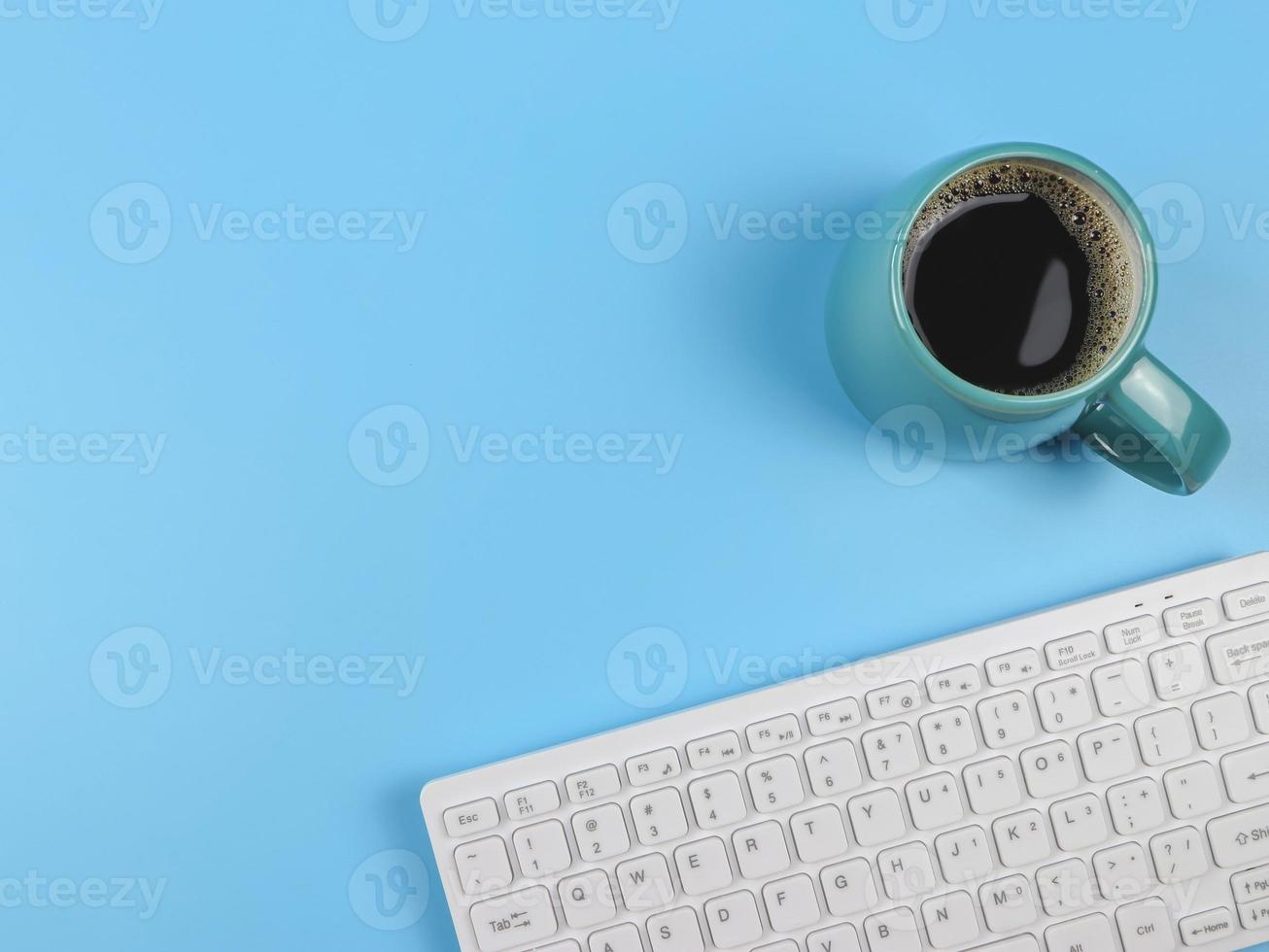 flat lay of computer keyboard, blue cup of black coffee on blue  background with copy space for text. Feminine workplace , Morning routine. photo