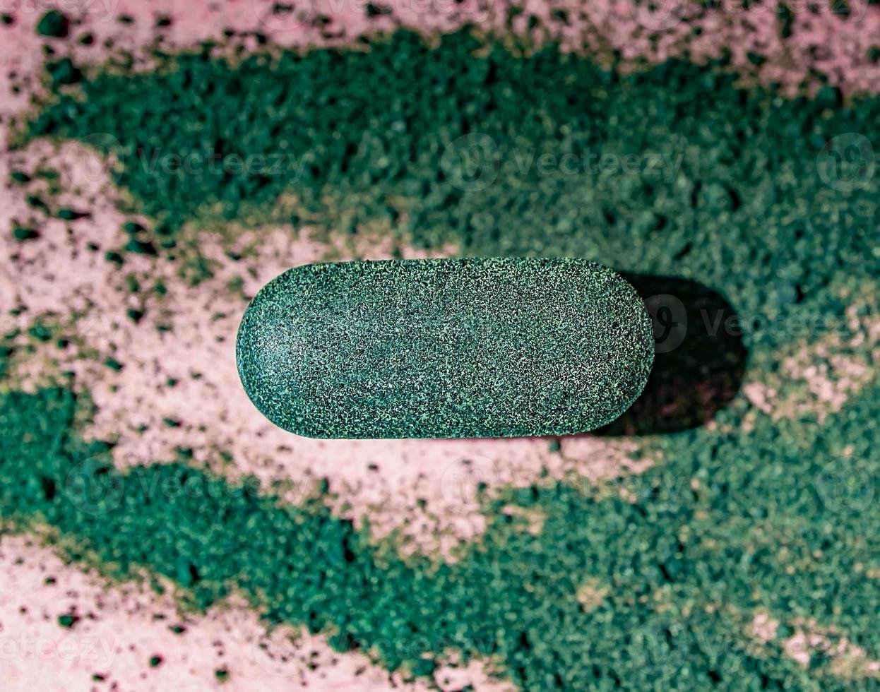 Close-up chlorella or spirulina tablet among the powder on a pink background Nutritional supplement, detox superfood photo