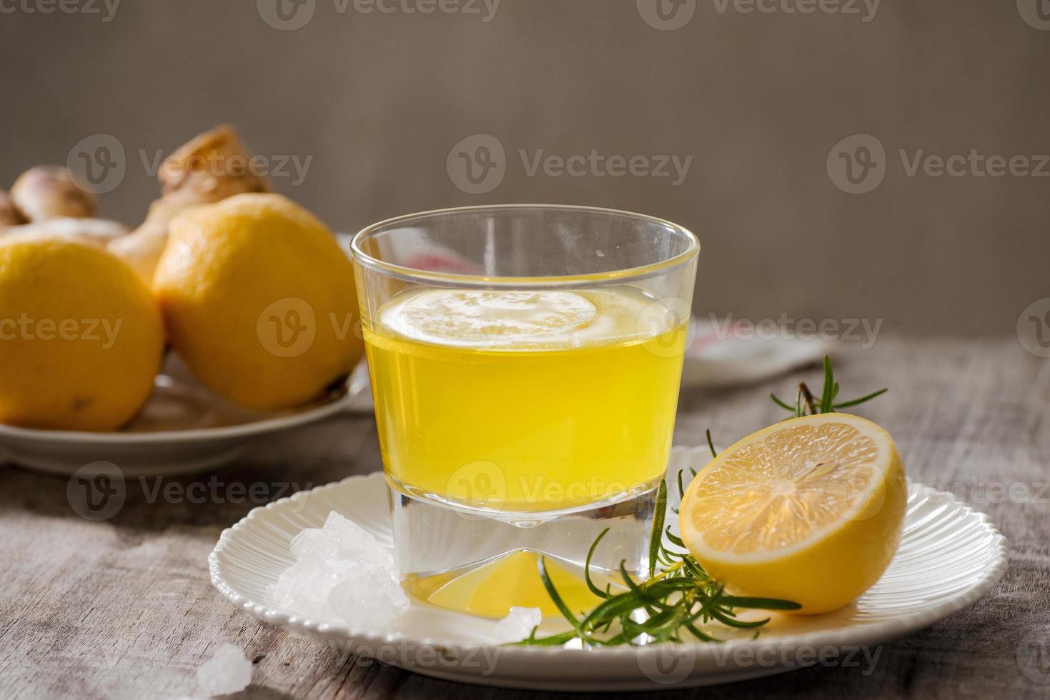 Ginger tea with lemon, ginger root and rosemarry on wooden background. Small glass transparent pitcher with hot drink. Seasonal beverages. Shallow DOF, selective focus, focus on top of pitcher. photo