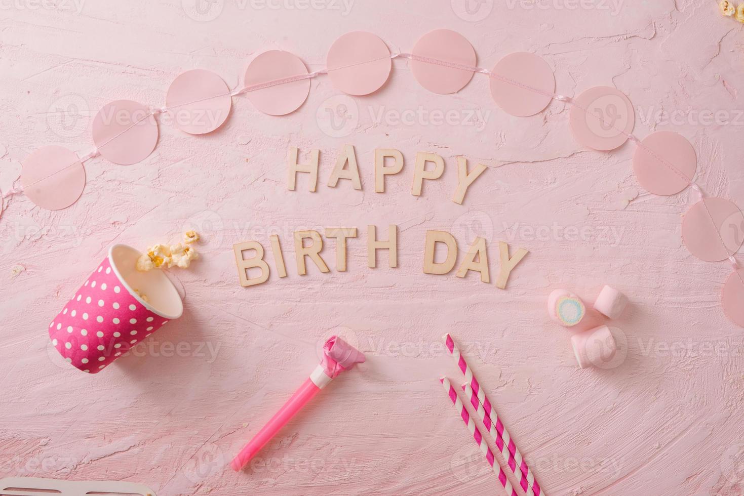Birthday party background, border of confetti, sweets, lollipops and gift on pink surface, copy space, top view photo