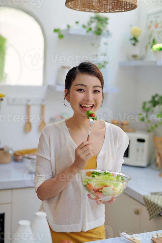 mujer hermosa joven comiendo ensalada fresca en casa foto