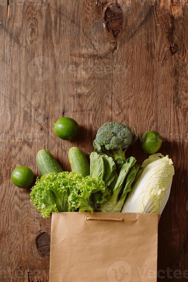 top view of green vegetables in shopping bag on wooden table photo