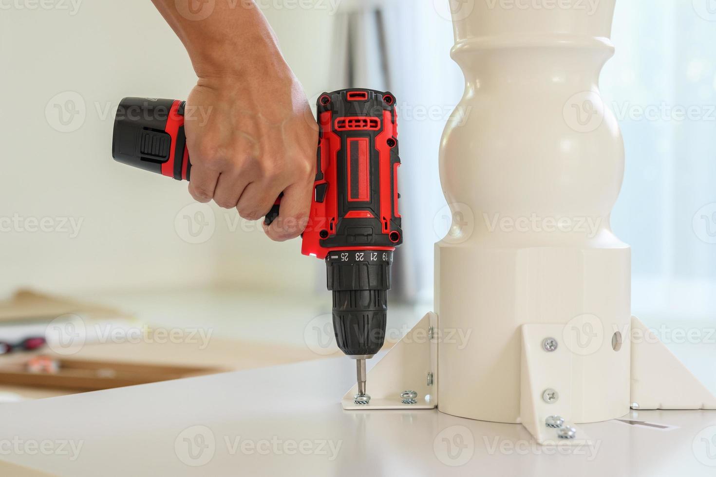 man assembling white table furniture at home using cordless screwdriver photo