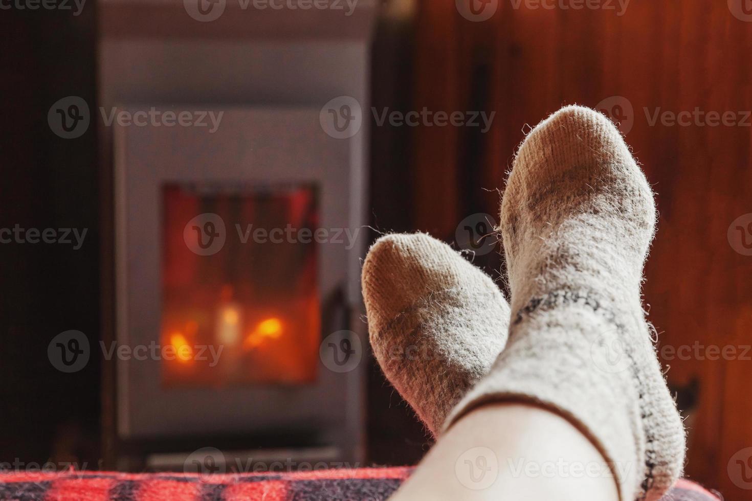 Feet legs in winter clothes wool socks at fireplace background. Woman sitting at home on winter or autumn evening relaxing and warming up. Winter and cold weather concept. Hygge Christmas eve. photo
