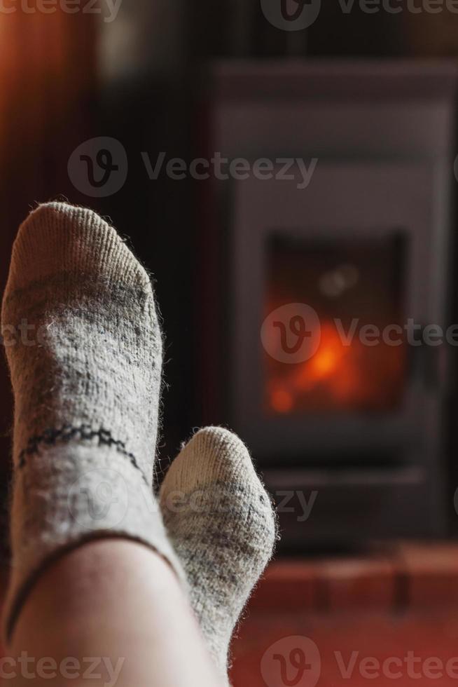 Feet legs in winter clothes wool socks at fireplace background. Woman sitting at home on winter or autumn evening relaxing and warming up. Winter and cold weather concept. Hygge Christmas eve. photo