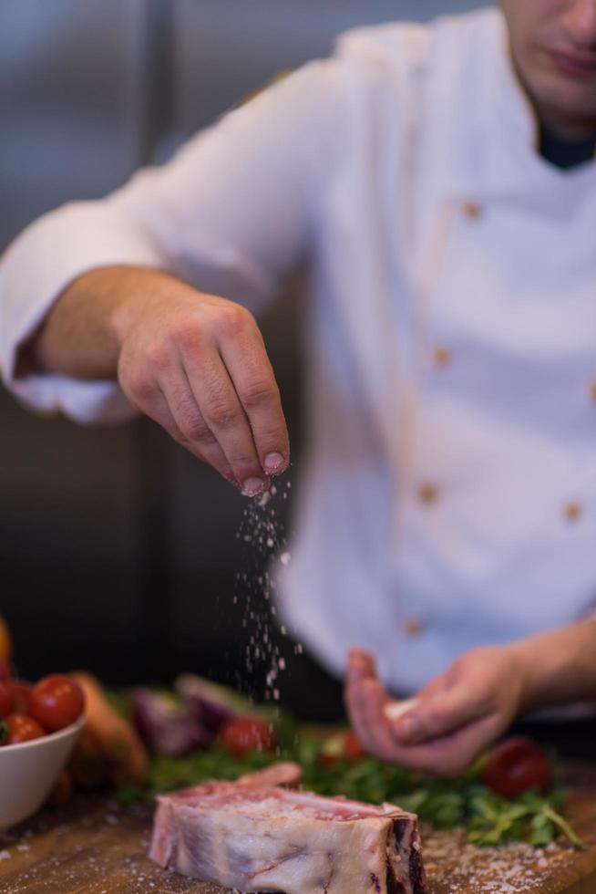 chef poniendo sal en una jugosa rebanada de bistec crudo foto