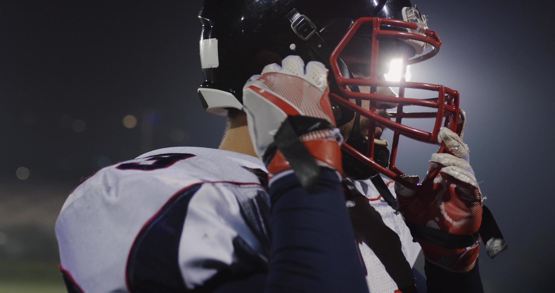 American Football Player Putting On Helmet on large stadium with lights in background photo