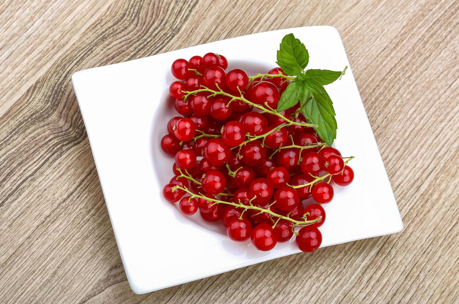 Red currants in a bowl on wooden background photo