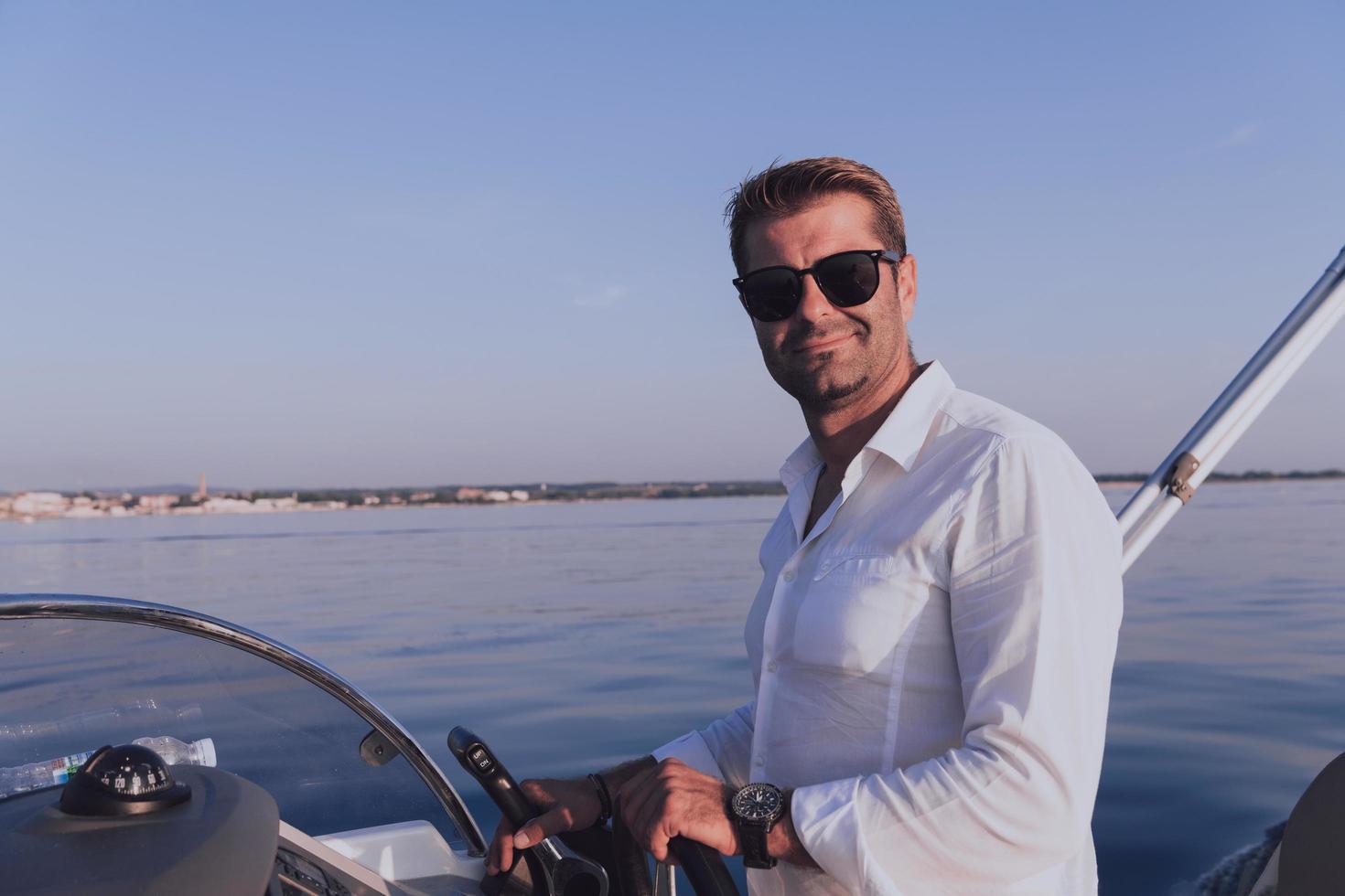 un hombre de negocios de alto nivel decidido con ropa informal y gafas de sol disfruta de sus vacaciones conduciendo un barco de lujo al atardecer. enfoque selectivo foto