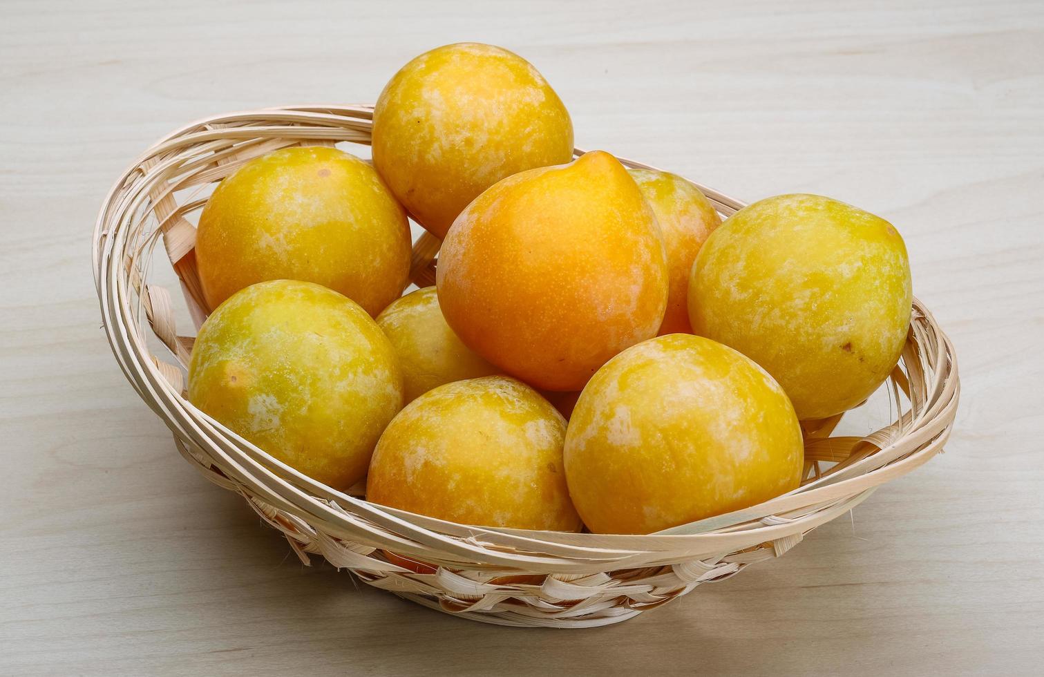 Yellow plums in a basket on wooden background photo
