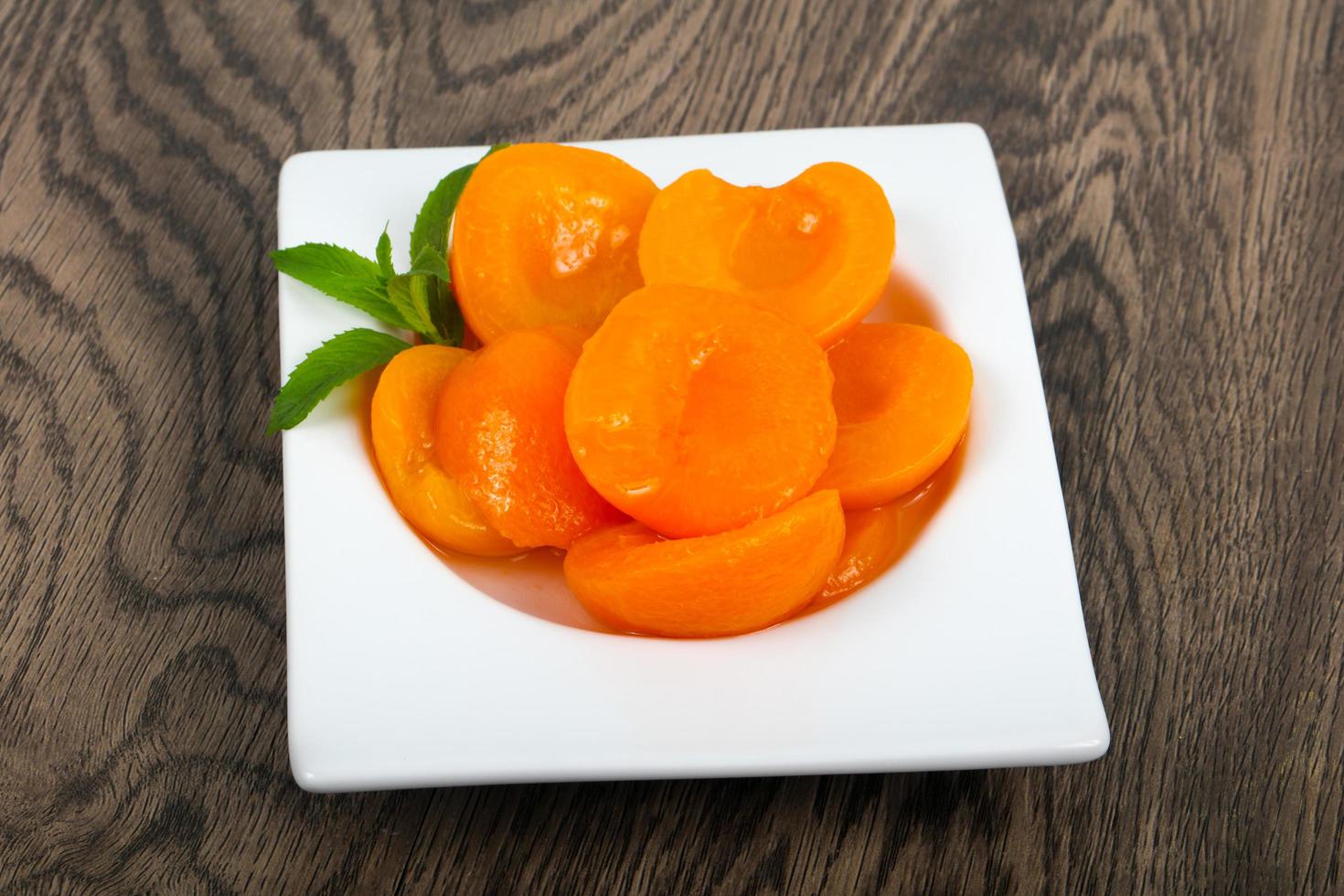 Canned apricots in a bowl on wooden background photo