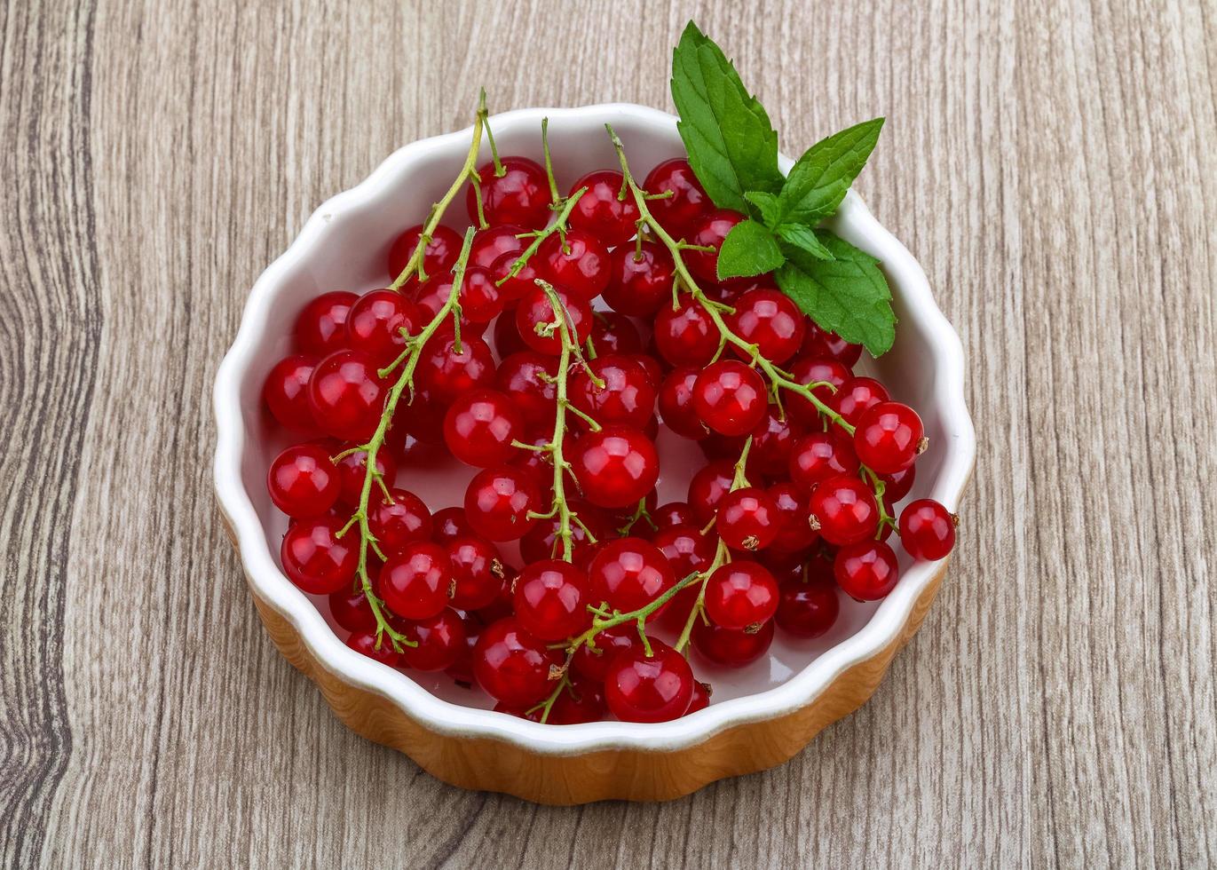 Red currants in a bowl on wooden background photo
