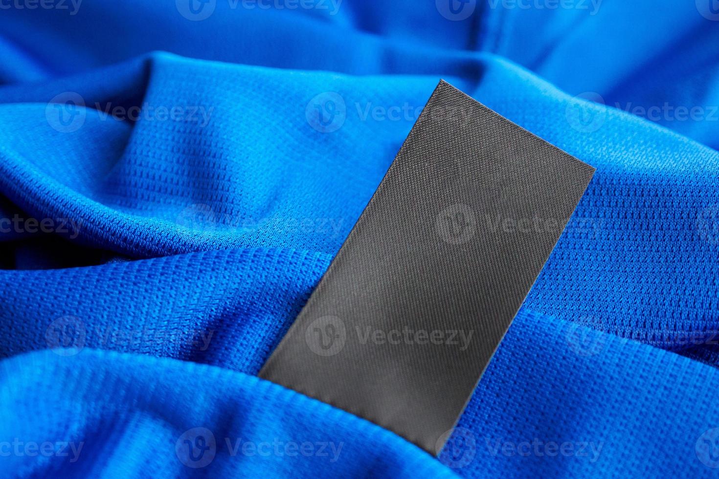 Black blank laundry care clothes label on blue jersey polyester sport shirt background photo