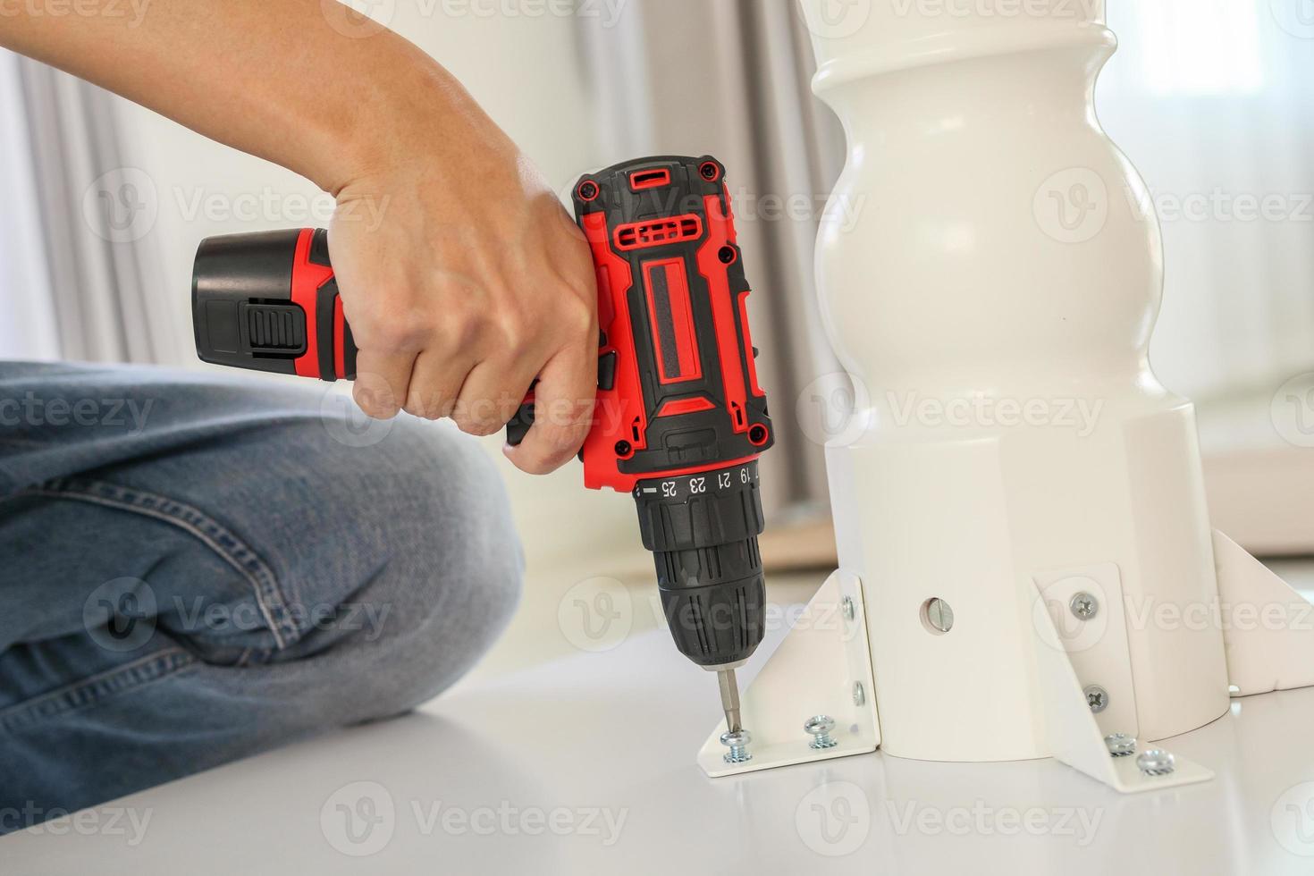 man assembling white table furniture at home using cordless screwdriver photo