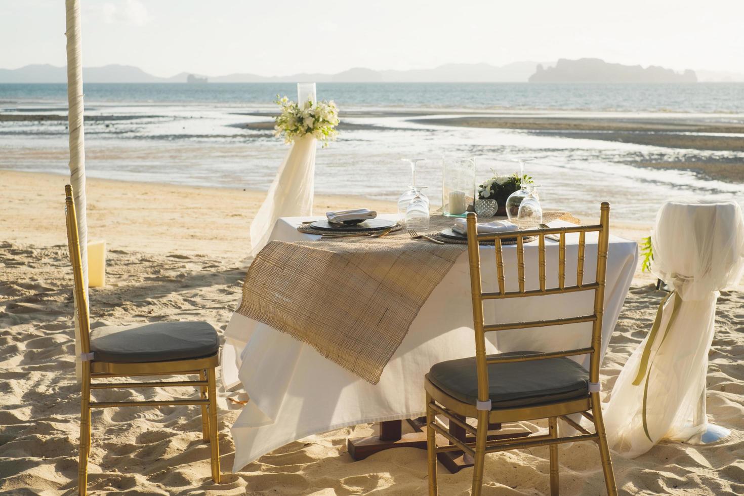 Beautiful table set up for a romantic dinner on the beach with  flowers and candles. Catering for a romantic date, wedding or honeymoon background. Sunset beach dinner. selected focus. photo